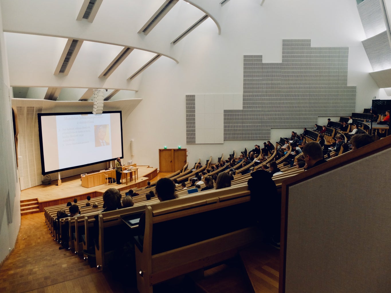 Students in an auditorium class at Aalto University in Espoo, Finland with a lecturer at the front.