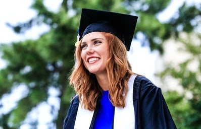 A woman smiles in her graduation cap and gown.