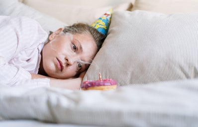 Woman lays in bed with a party hat on and a blown out candle in a donut.