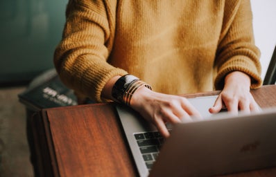 woman wearing yellow sweater typing on laptop