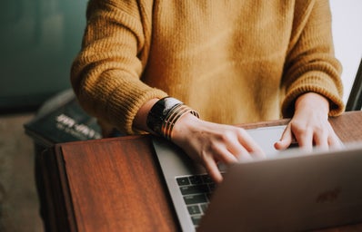 woman wearing yellow sweater typing on laptop
