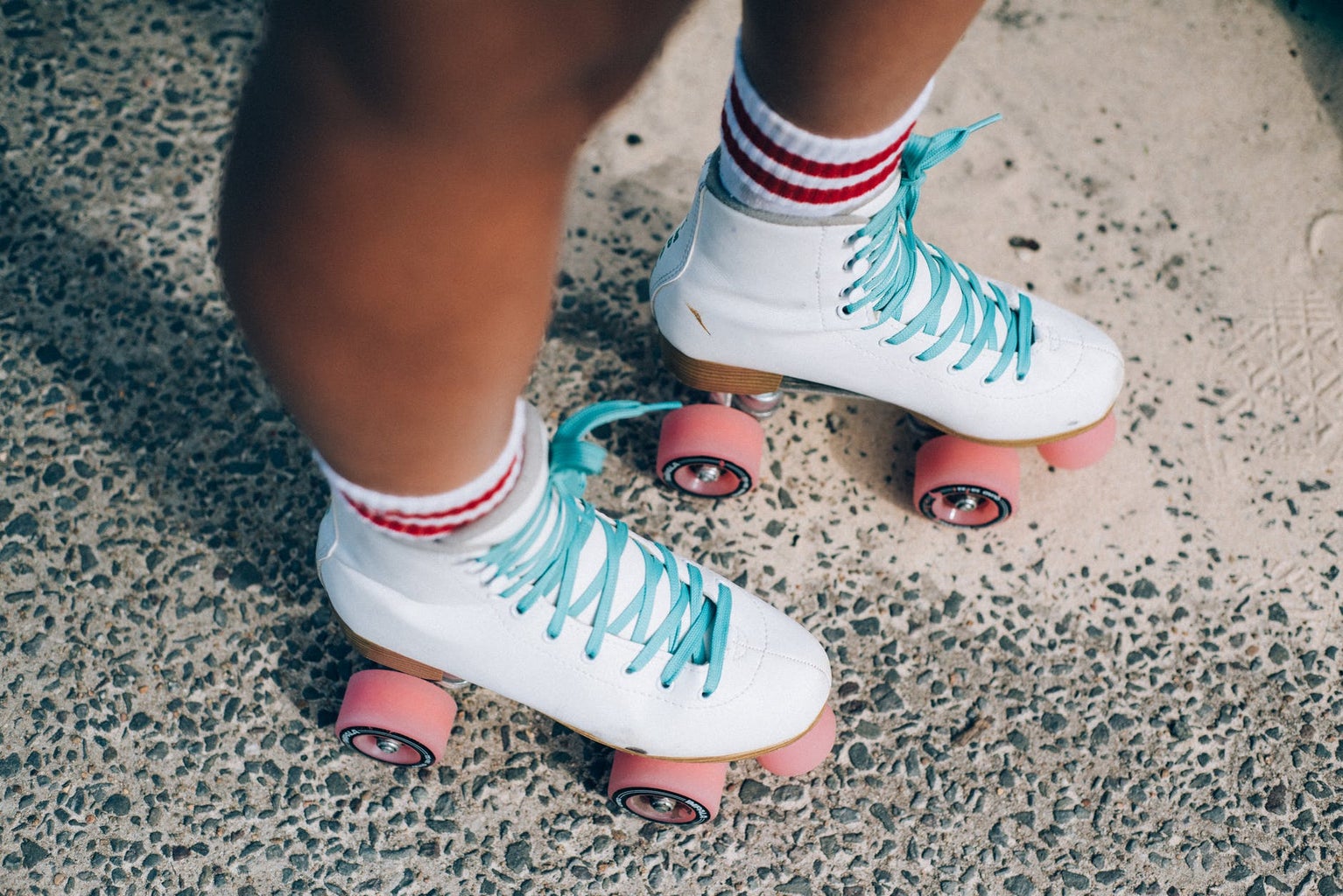white roller skates with light blue laces and pink wheels; white socks with two red stripes on each.