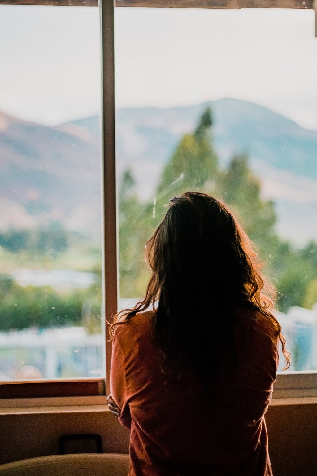 Woman with her hair down staring out the window at mountains.