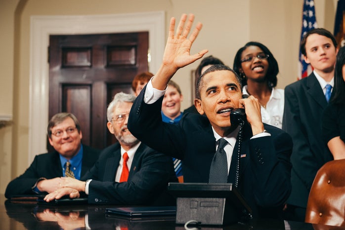 Barack Obama waving at a desk while on the phone