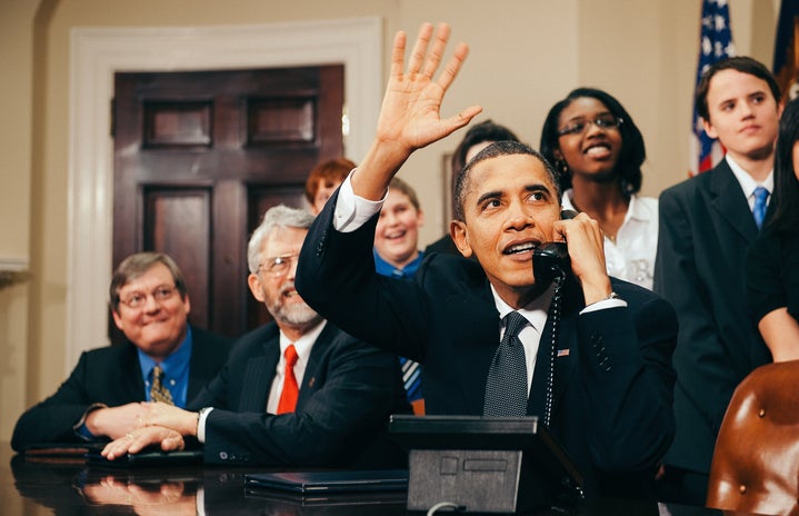 Barack Obama waving at a desk while on the phone