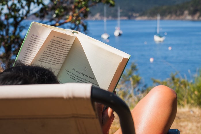 person reading book in chair relaxing with ocean in the distance