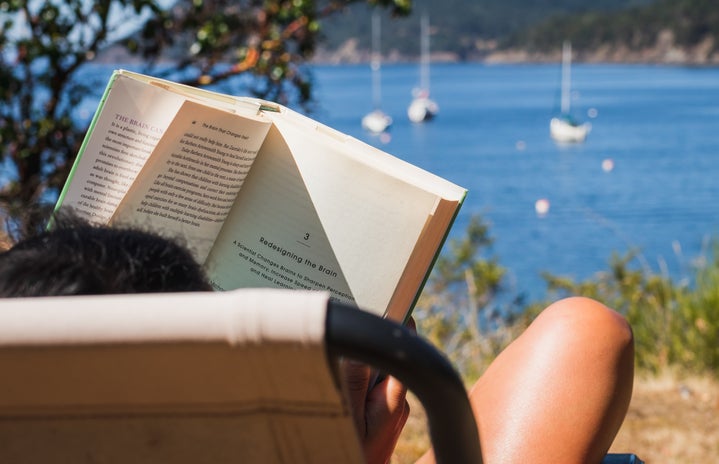 person reading book in chair relaxing with ocean in the distance