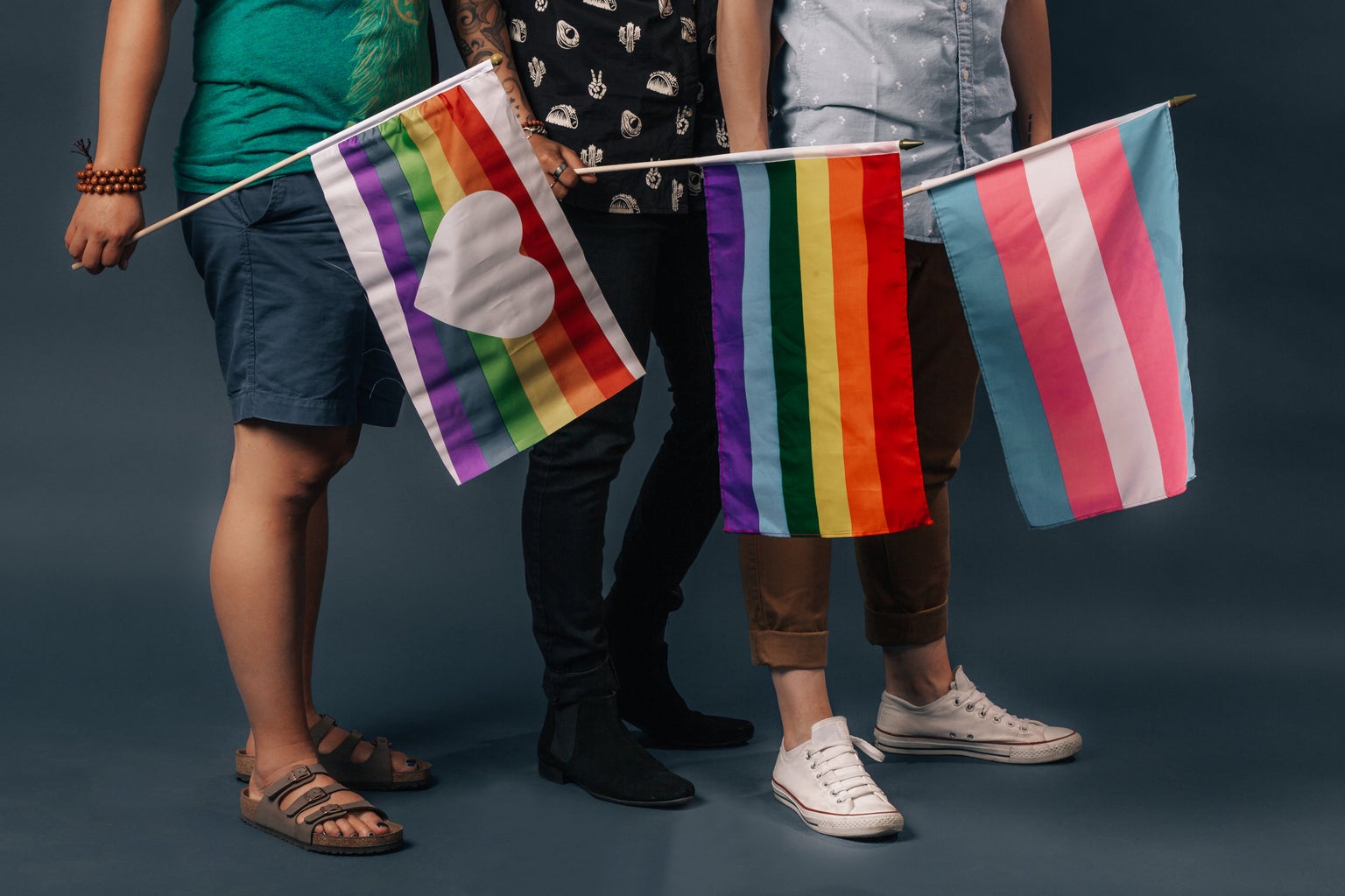 Three people holding three different LGBTQ+ pride flags.