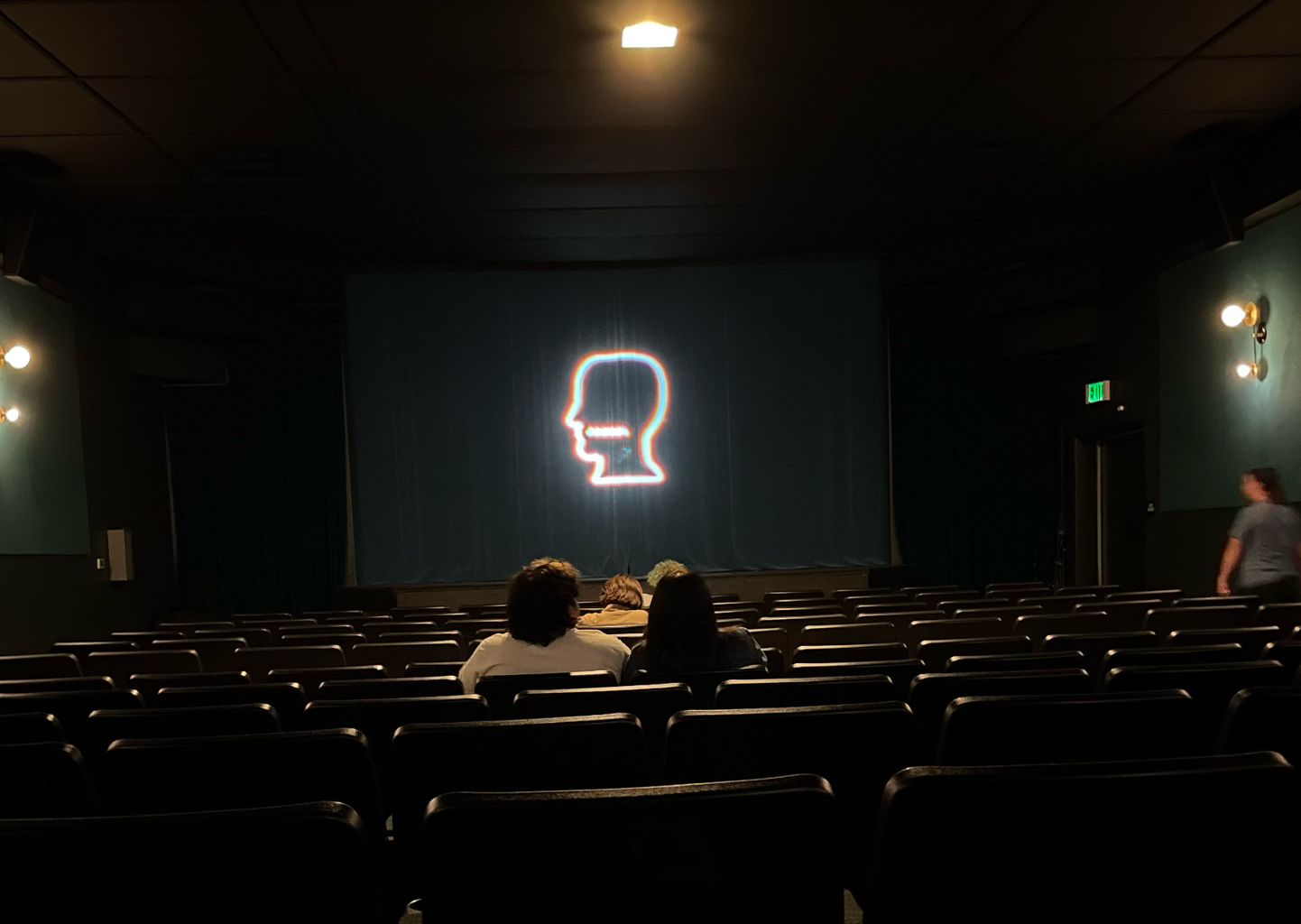Dark movie theater with a black stage and a side profile silhouette projected onto it.
