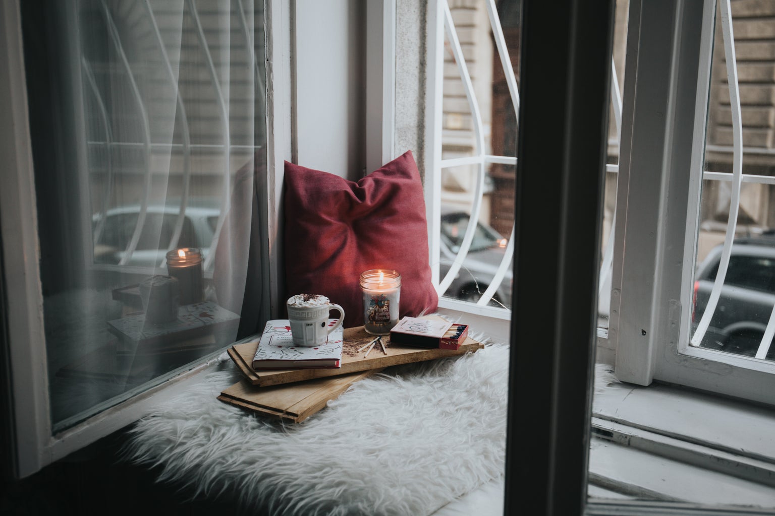 photo of a candle, matches, and a mug resting on pillows by a window