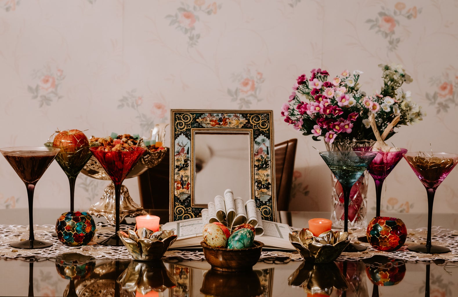 A table filled with cups, flowers, empty frames, flowers, lit candles, and colorful eggs.