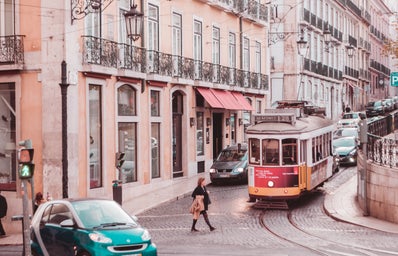woman wearing black coat passing on road while tram is near during daytime in Lisbon, Portugal