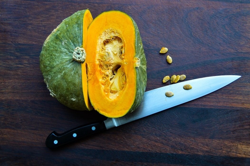 sliced green and orange squash with knife on wooden board
