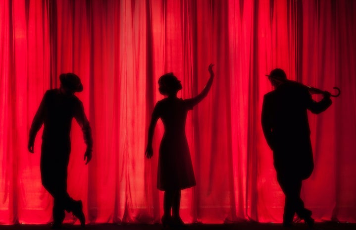 three figures in front of a red curtain