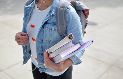 College student in denim holding textbook and earphones