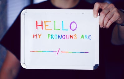 person holding a whiteboard written \"hello my pronouns are\" in colored letters