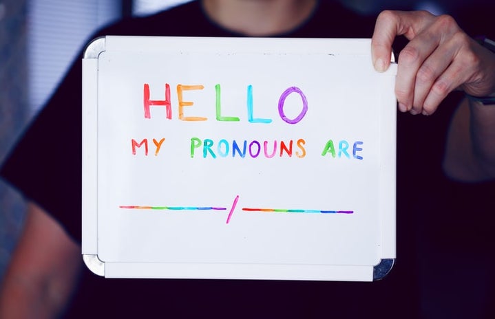 person holding a whiteboard written \"hello my pronouns are\" in colored letters