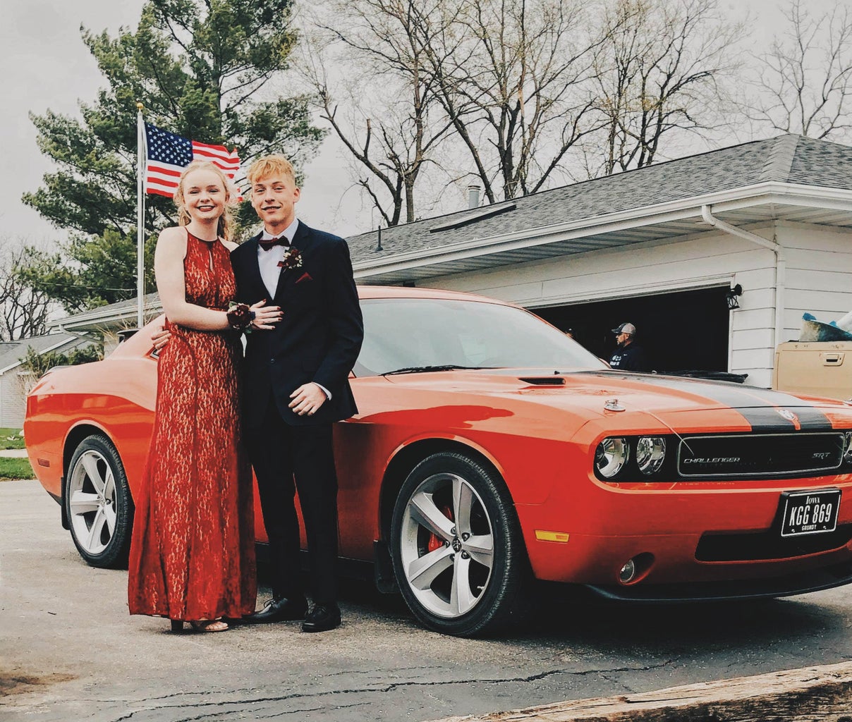 Brianna Strohbehn in her red Prom dress next to her boyfriend and a red vehicle.