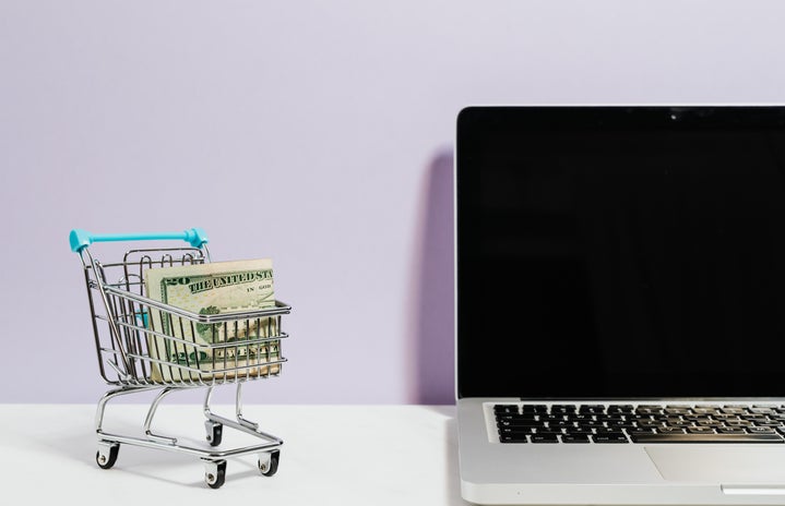 mini shopping cart with money in it next to a laptop