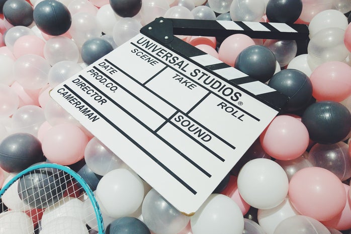 a movie clapperboard sitting on top of pink, black, white, and clear balloons