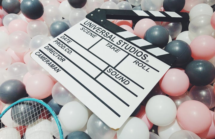 a movie clapperboard sitting on top of pink, black, white, and clear balloons