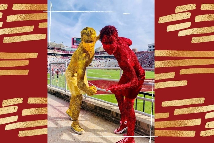two guys covered in gold and garnet glitter posing in front of football field