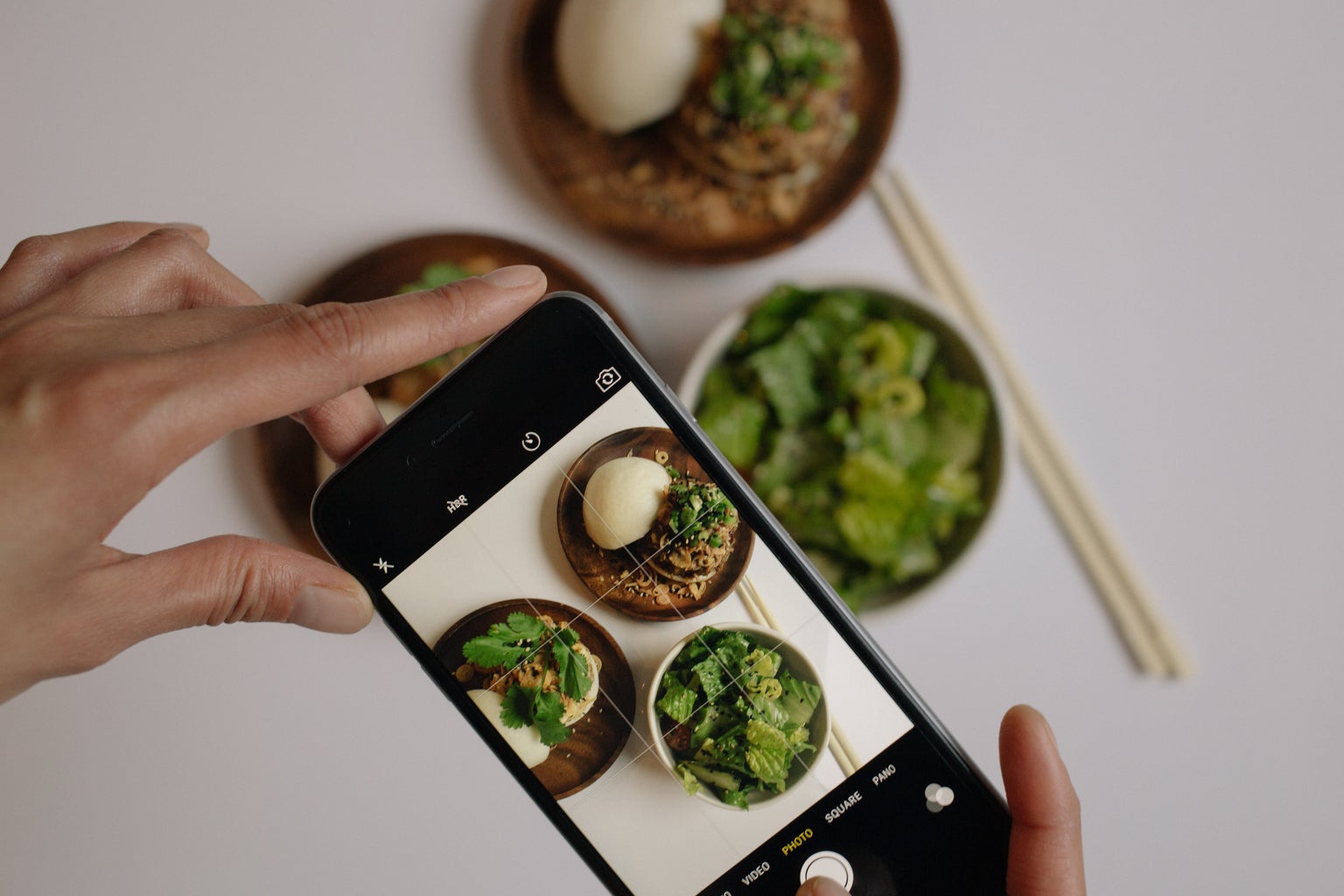 A person\'s hands taking a photo of 3 bowls of food
