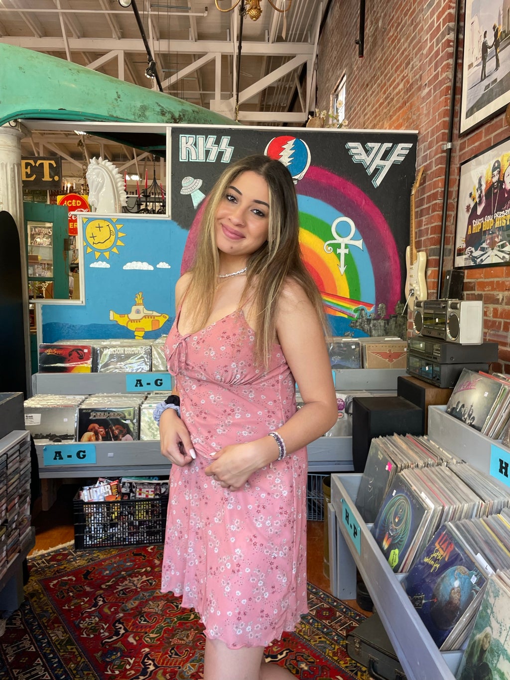 Alexis McDonald in a pink dress in a record store with rainbow art behind her