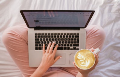 person holding coffee and typing on laptop