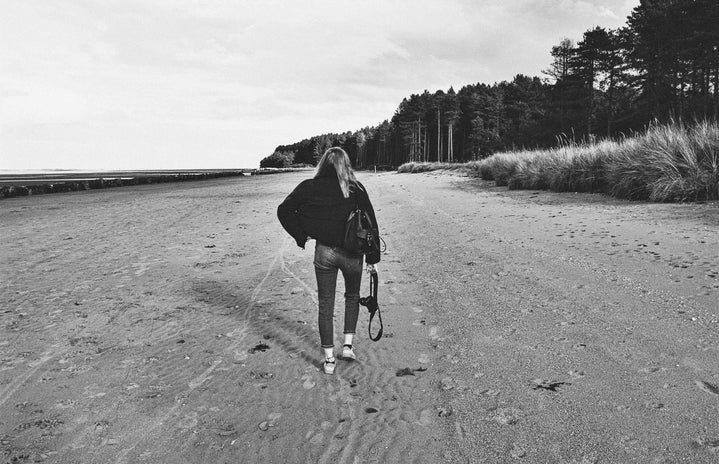 black and white photo of woman walking away on a beach