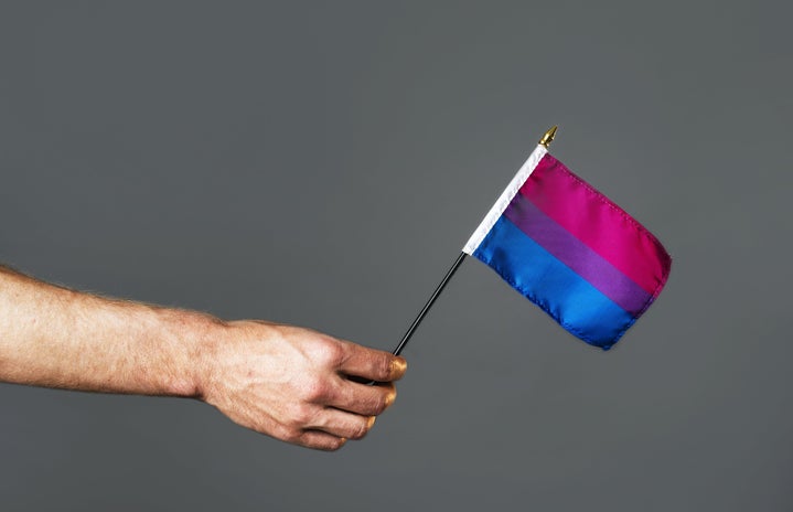 Close up of a person\'s hand, holding a bisexual pride flag.