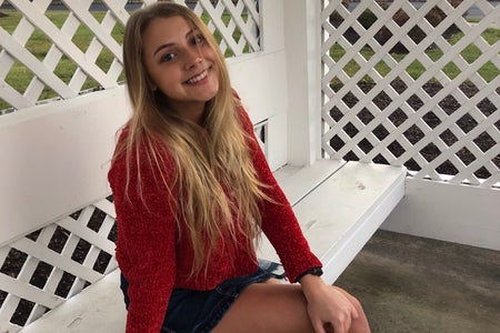Young white woman, Tara Teipel, wearing a red top and sitting on a white bench.