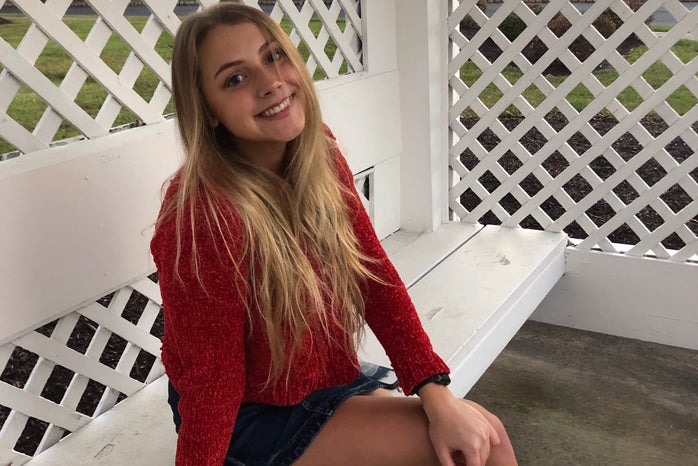 Young white woman, Tara Teipel, wearing a red top and sitting on a white bench.