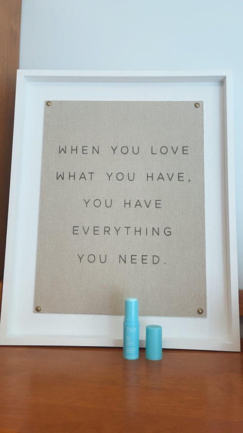 This is an image of a Tula Eye Cream bottle with the cap off on display in front of a motivational sign