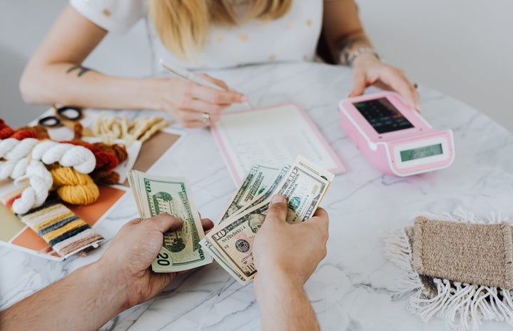 Hands counting dollar bills with woman using calculator in background