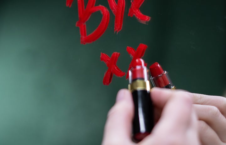 Woman writing the word "Bye" on a mirror with red lipstick