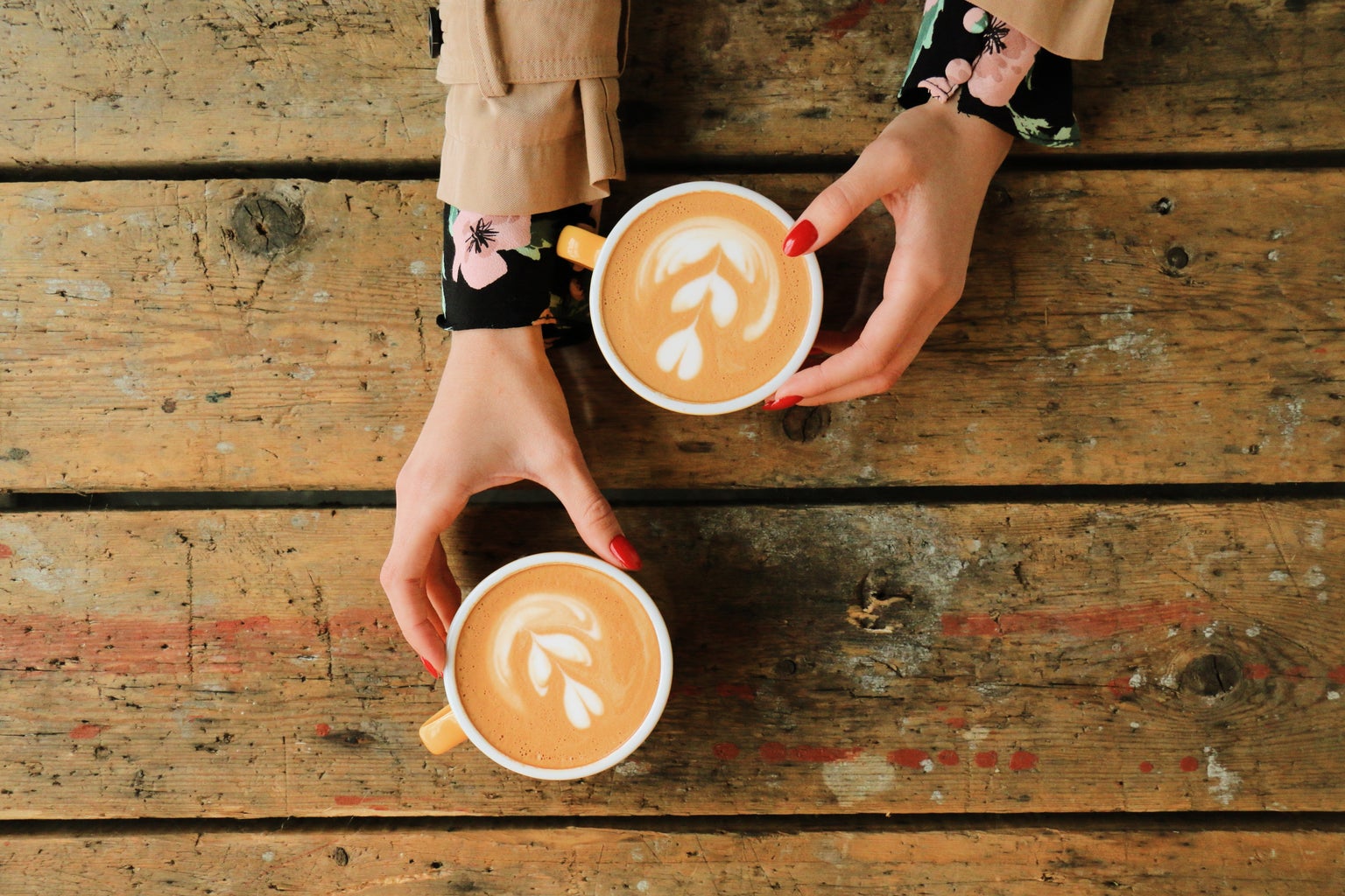 two hands belonging to a single person reaching for two coffee cups on a table