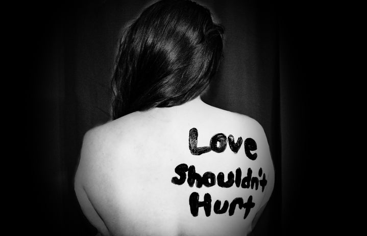 A woman\'s bare back painted in black lettering saying \"Love Shouldn\'t Hurt\"
