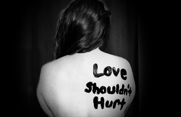 A woman\'s bare back painted in black lettering saying \"Love Shouldn\'t Hurt\"