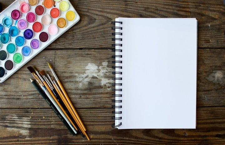 watercolor set with paintbrushes and notebook on wooden table