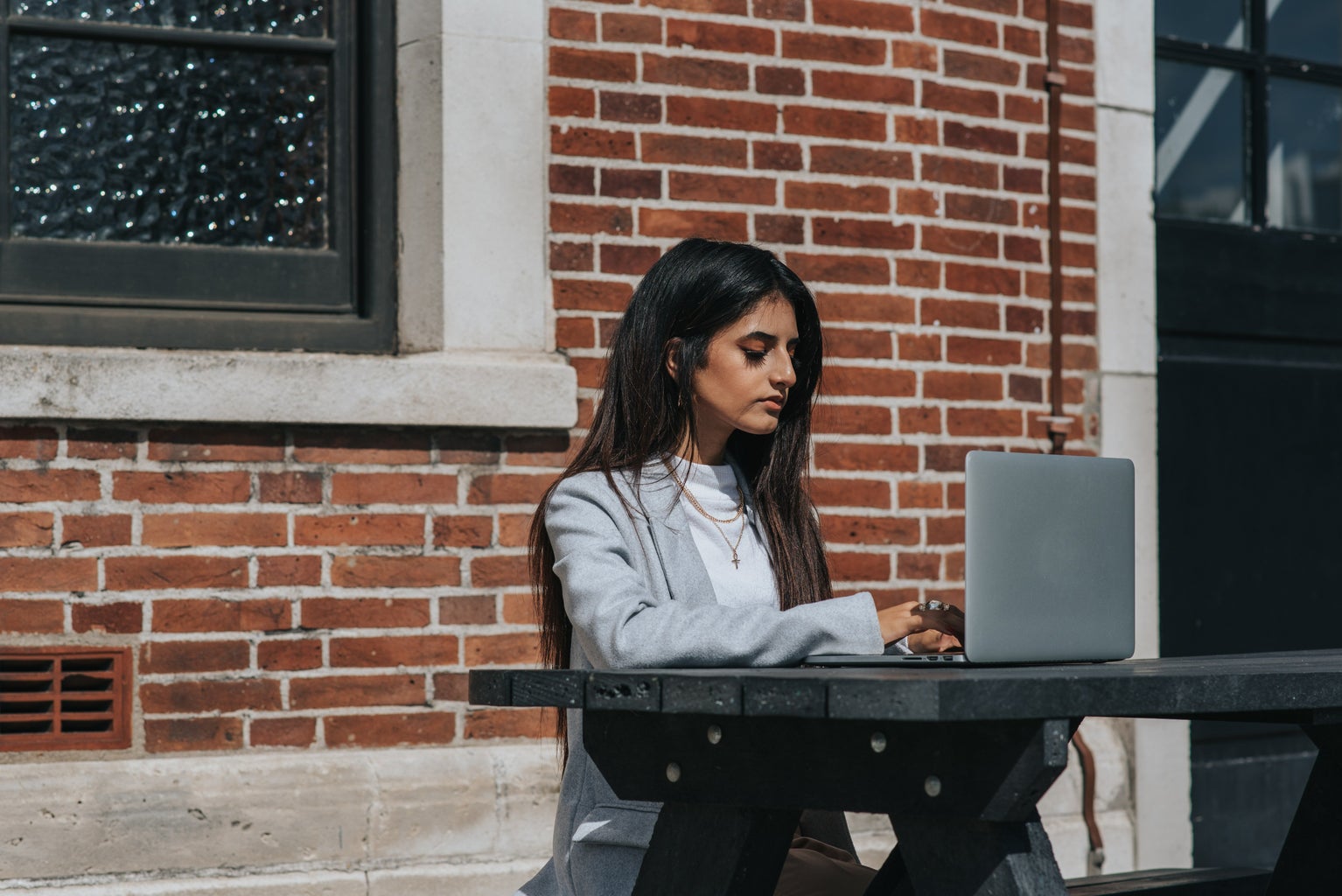 Woman sitting in front of a brick wall at a table with her laptop in front of her.