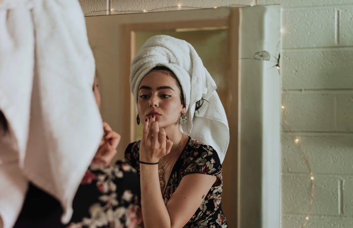 woman putting on makeup in front of mirror