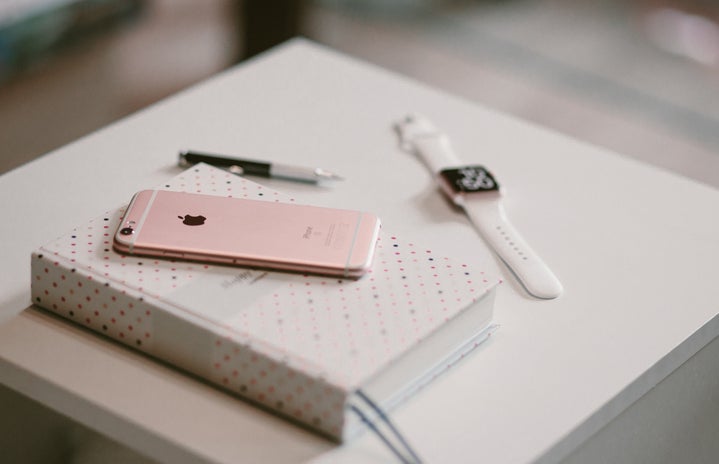 Rose gold smartphone on top of white white covered book with smartwatch