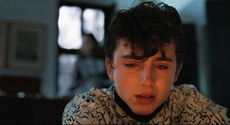 Character Elio is sitting in front of the fireplace crying.