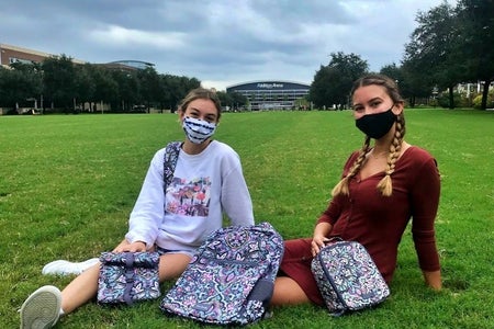 two students sitting on the grass with book bags