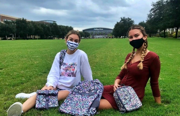 two students sitting on the grass with book bags