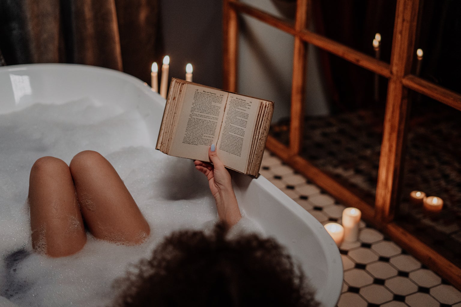 A woman in a bathtub reads a book.