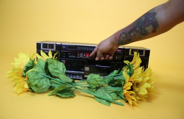 person with tattoo on arm pressing button on radio surrounded with flowers