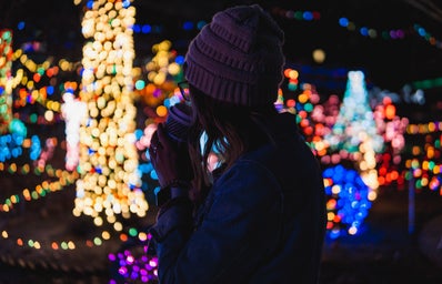 Girl sipping drink in front of Christmas lights.