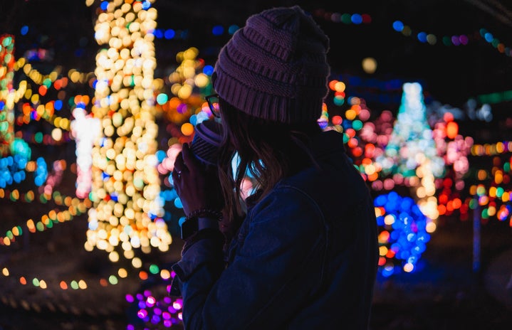Girl sipping drink in front of Christmas lights.